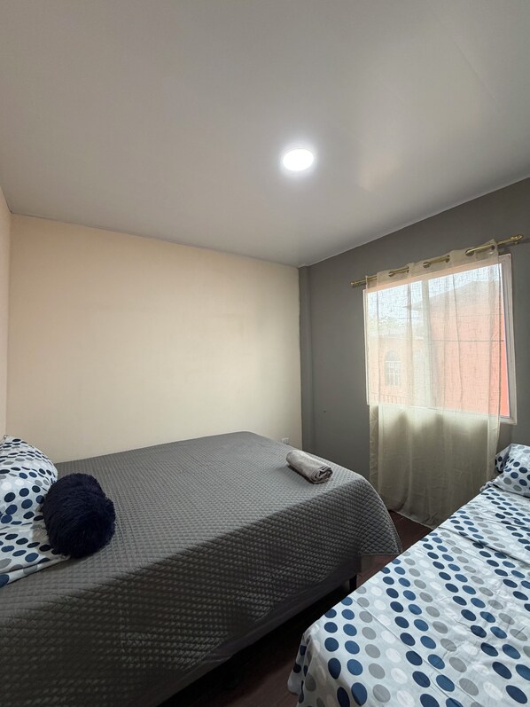 Una habitación con dos camas, una ventana con cortinas y una lámpara en el techo.