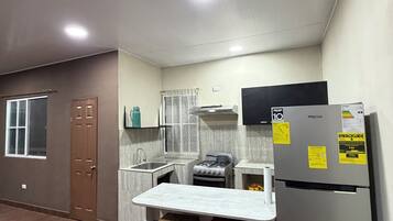 Cocina compacta con refrigerador, estufa y lavabo. Hay dos taburetes y una mesita.