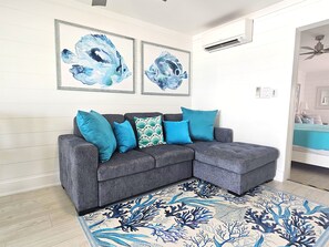 A grey sectional sofa with blue and teal cushions, a blue and white coral-patterned rug, and two abstract blue paintings on the wall. - Miramar Beach 1BR • Prv Beach, Beach Service, Golf (Miramar Beach)