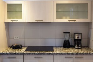 Una cocina con armarios de madera clara, encimera de granito, licuadora y cafetera.