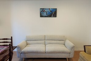 A living room with a beige sofa, a wooden dining table with a patterned tablecloth, and a painting on the wall. - Wonderful 2-bedroom apartment in the heart of Quito (Quito)
