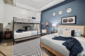 A room with a bunk bed, a large bed, a checkered rug, and a wall with three round mirrors and a framed picture. - The Bentley Collection - The Rhythm Loft (Dallas)