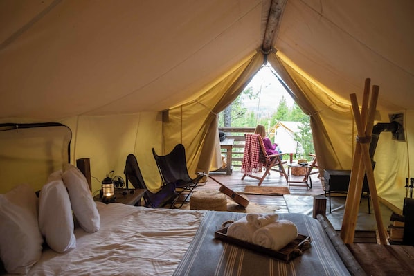 A tent with a bed, chairs, a table, and a view of the outdoors.
