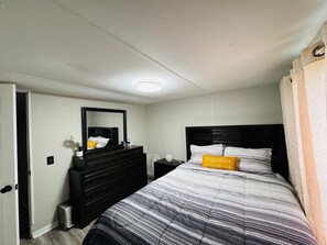 A bedroom with a bed, a dresser, a nightstand, a mirror, and a door. - Cozy 2-bedroom house in beautiful Bartow: 20m to Legoland, 1h to Disney & TPA (Bartow)