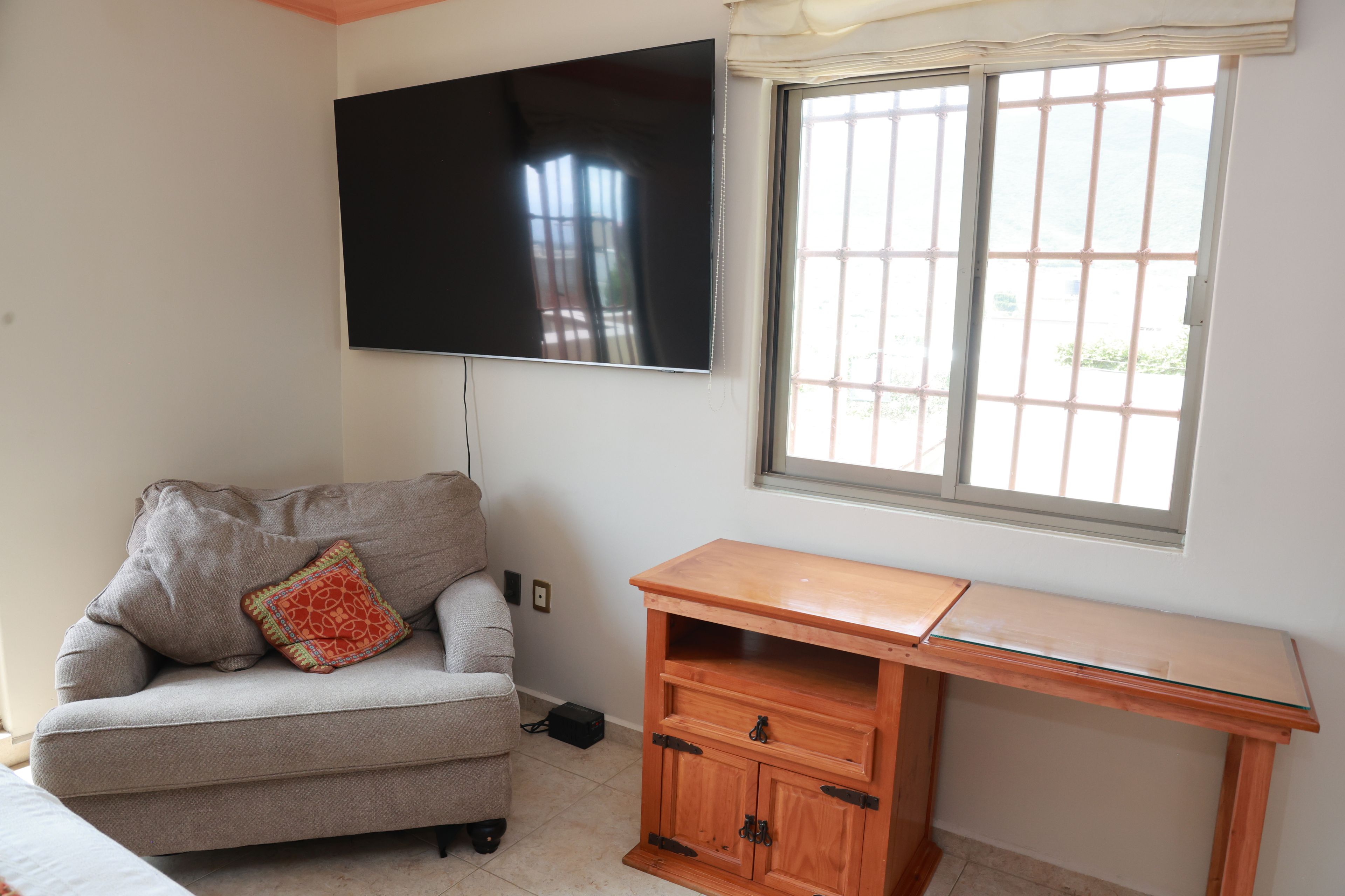 Un salon comprenant un canapé, un téléviseur fixé au mur, un bureau en bois et une fenêtre donnant sur un beau paysage.