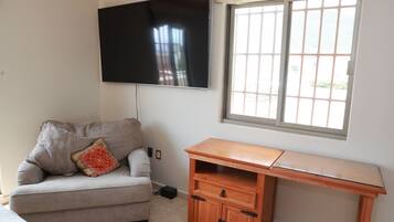 A living room with a sofa, a TV mounted on the wall, a wooden desk, and a window with a view.
