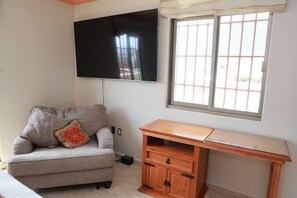 A living room with a sofa, a TV mounted on the wall, a wooden desk, and a window with a view.