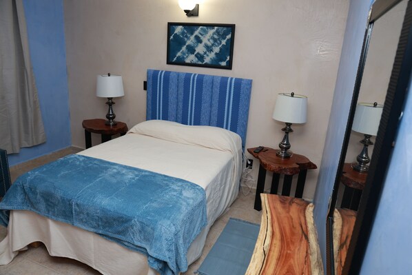 A hotel room with a bed, two bedside tables, a nightstand, a wall-mounted lamp, a painting, and a mirror. - La Casa de May, perfect for families and friends (San Andrés Huayápam)