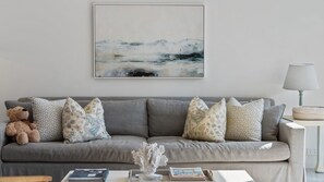A neutral-toned living room with a grey sofa, patterned cushions, a decorative coral piece, and a framed abstract painting on the wall. - Catherine Hill Bay - Ocean Views & Coastal Living (Catherine Hill Bay)