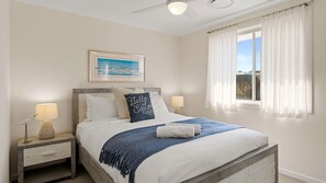 A bedroom with a bed, nightstands, a framed picture, a window with curtains, and a ceiling fan. - Catherine Hill Bay - Ocean Views & Coastal Living (Catherine Hill Bay)