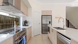 A modern kitchen with a stove, oven, coffee machine, refrigerator, and dishwasher. - Catherine Hill Bay - Ocean Views & Coastal Living (Catherine Hill Bay)