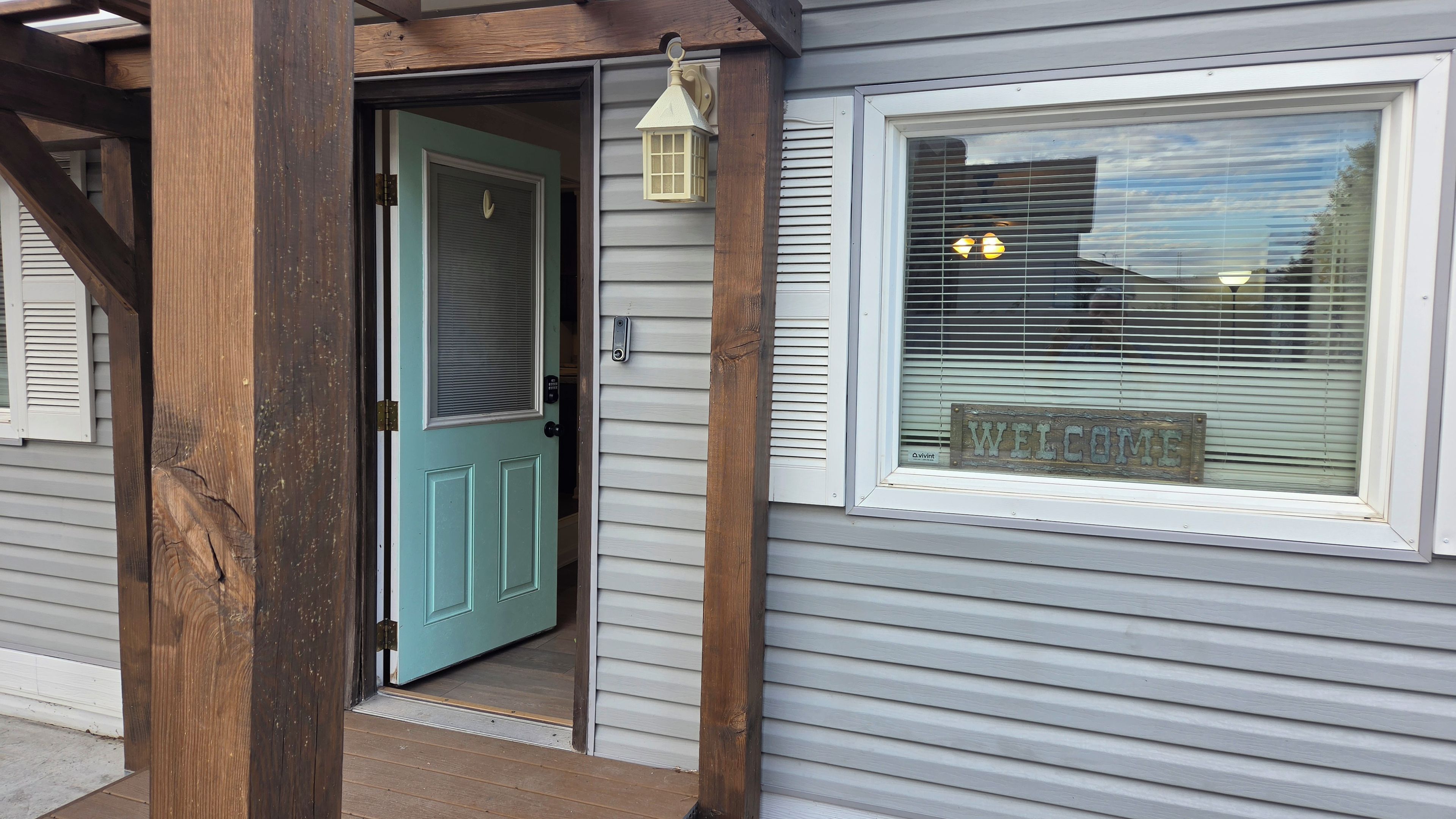 Una casa con puerta azul, una ventana con el letrero 'WELCOME' y un porche de madera.