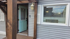 Una casa con puerta azul, una ventana con el letrero 'WELCOME' y un porche de madera.