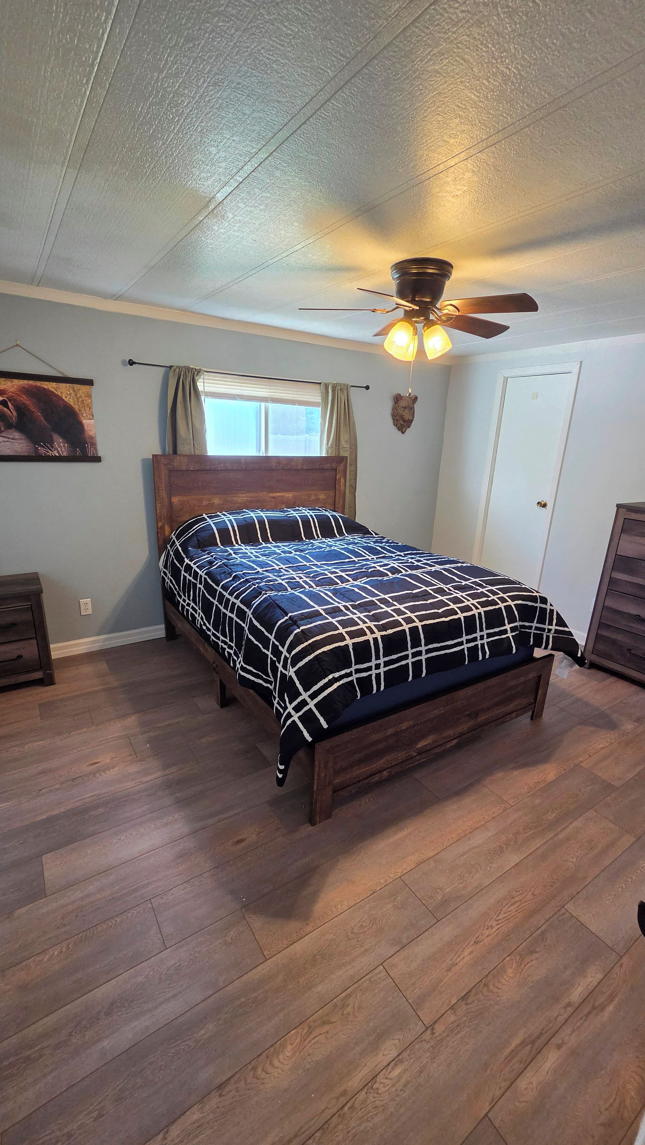 Un dormitorio con cama de madera, ventilador de techo, ventana con cortinas y una puerta.