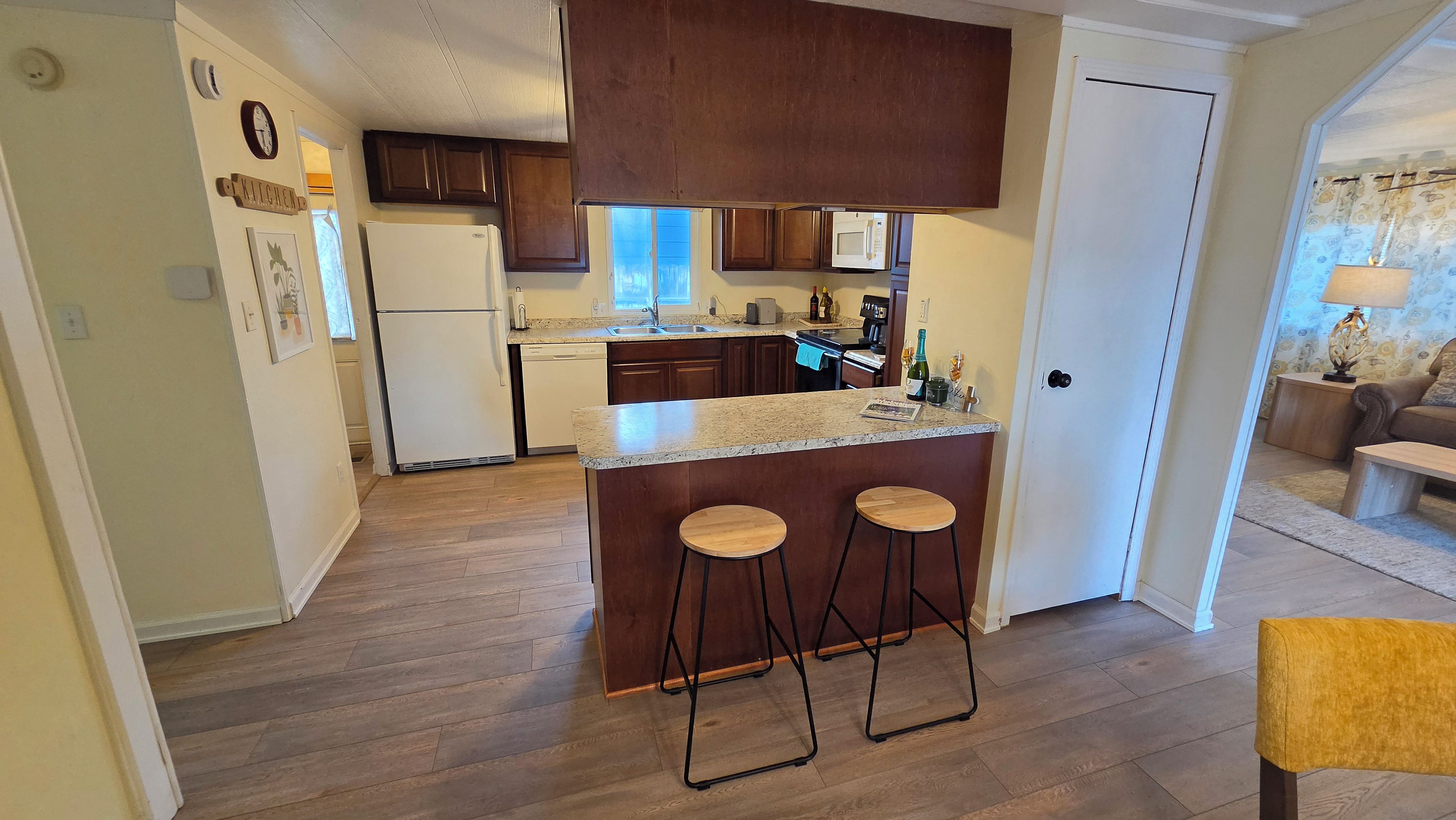 A compact kitchen with wooden cabinets, a refrigerator, a microwave, and a bar area with stools.