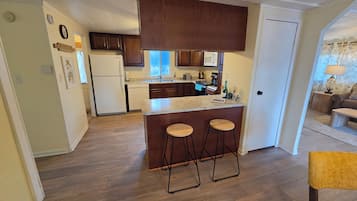 A compact kitchen with wooden cabinets, a refrigerator, a microwave, and a bar area with stools.