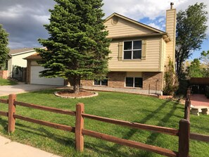 A two-story house with a brick facade, a front yard with a tree, and a wooden fence. - Gorgeous 3-bedroom house in tranquil Colorado Springs neighborhood (Colorado Springs)