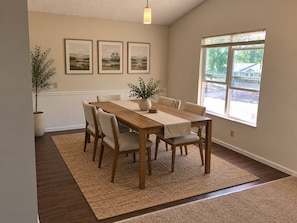Een eetgedeelte met een houten tafel, zes stoelen, een potplant en drie foto's in lijsten aan de muur.