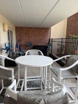 A patio area with a round table and white chairs, a brick wall, and a black metal fence. - 2-bedroom condo in serene South Padre Island just steps from the beach. (South Padre Island)