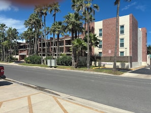 A multi-story hotel with a brick facade, palm trees, and a clear sky. - 2-bedroom condo in serene South Padre Island just steps from the beach. (South Padre Island)