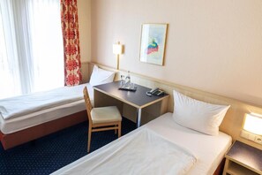 Ein Hotelzimmer mit zwei Betten, einem Schreibtisch, einem Sessel, einer Lampe und einem Bild an der Wand.