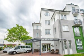 Ein mehrstöckiges Hotel mit überdachter Einfahrt, einem geparkten Auto davor und einem Baum in der Nähe.