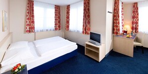 Ein Hotelzimmer mit einem Bett, einem Schreibtisch mit Computer, einem Fernseher und einer Lampe.