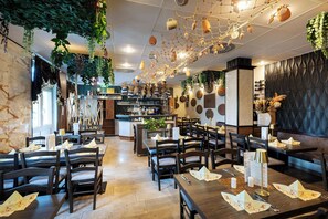 Ein Restaurantinneres mit Holztischen und -stühlen, hängenden Pflanzen und einer Küche im Hintergrund.