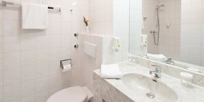 Ein modernes Badezimmer mit Toilette, Waschbecken, Spiegel, Dusche und Handtuchhalter.