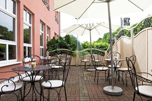 Eine Terrasse im Freien mit Tischen und Stühlen, einem Backsteinboden und einem Gebäude mit großen Fenstern.