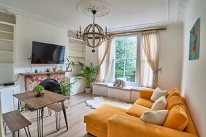 Un salon avec un canapé, un téléviseur, une cheminée et une fenêtre avec des rideaux.