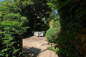 Eine Garten-Terrasse mit Tisch und Stühlen, umgeben von üppiger Vegetation und einem großen Baum.