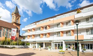Ein mehrstöckiges Hotel mit Balkonen, einem Glockenturm und einem Gartenbereich mit Topfpflanzen.