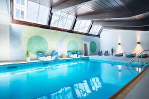 Ein Innenpool mit Dachfenster, blauen Fliesen und Liegestühlen.