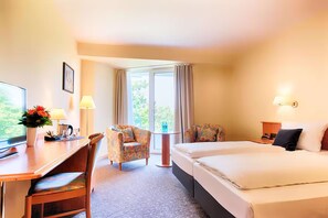 Ein Hotelzimmer mit Bett, Schreibtisch, Stuhl, Lampe und einem Fenster mit Vorhängen.