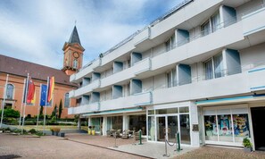 Ein mehrstöckiges Hotel mit Balkonen, einem Glockenturm und Flaggen.