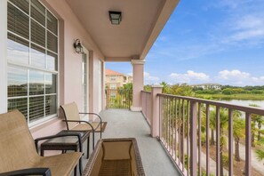 A balcony with a view of a lake, a chair, a table, and a lamp. - Amazing 4BR at Vista Cay with Gorgeous Lake View (Orlando)