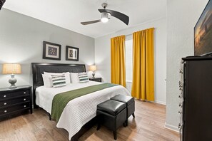 A bedroom with a bed, nightstands, a desk, a chair, a ceiling fan, and a window with curtains. - Amazing 4BR at Vista Cay with Gorgeous Lake View (Orlando)
