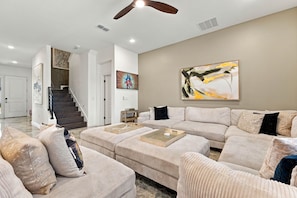 A spacious living room with a sectional sofa, a coffee table, and a large abstract painting on the wall. - Stunning 6BR, Private Pool, Prime Location (Orlando)