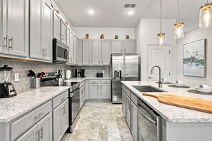 A modern kitchen with stainless steel appliances, white cabinetry, a marble countertop, and pendant lighting. - Stunning 6BR, Private Pool, Prime Location (Orlando)