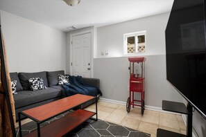 A living room with a grey sofa, a wooden coffee table, a red cart, and a TV. - Family 4BR DC Retreat w/ Theater & Game Room (Arlington)