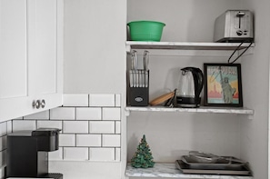 Een keuken met witte kastjes, een koffieapparaat, een groene mand, een broodrooster, een waterkoker, een fotolijstje en een kleine kerstboom.