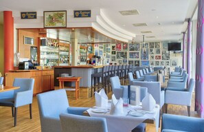Ein Restaurant mit Barbereich, verschiedenen Sitzgelegenheiten und einer Wand mit gerahmten Bildern.