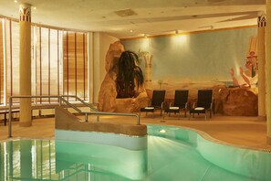 Una piscina interior con un mural de pared de roca, zona de estar y una escalera que lleva a la piscina.