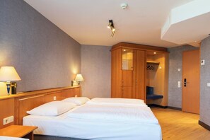 Habitación de hotel con cama, lámparas de noche, armario de madera y un banco.