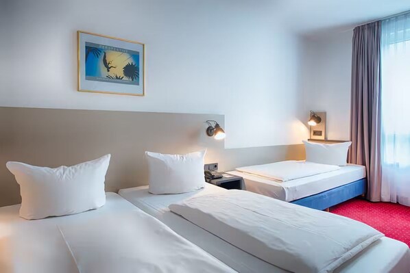 Ein Hotelzimmer mit zwei Betten, einem gerahmten Bild an der Wand und einem Fenster mit Vorhängen.