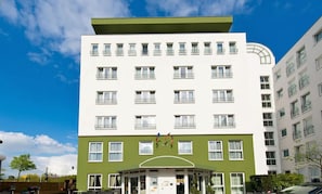 Ein mehrstöckiges Hotel mit einer grün-weißen Fassade, zahlreichen Balkonen und einem zentralen Eingang mit Flaggen.