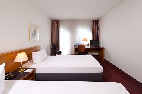 Ein Hotelzimmer mit einem Bett, Nachttischen, einem Schreibtisch, einem Sessel, einem Fernseher und Vorhängen.