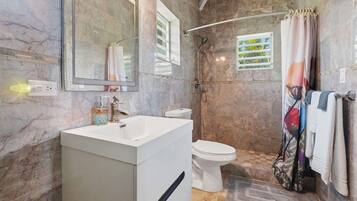 A bathroom with a marble wall, a white sink, a toilet, and a shower area.
