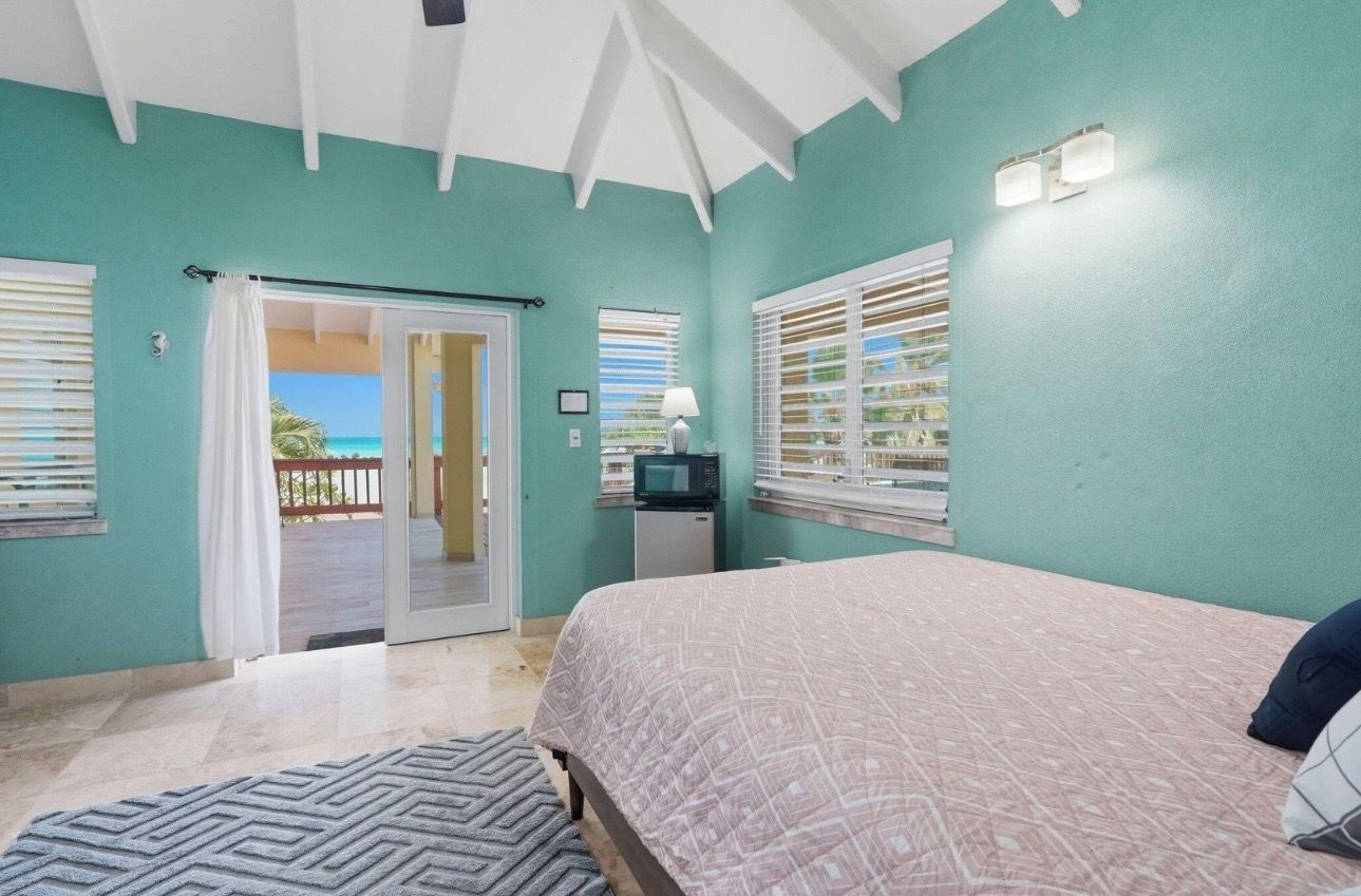 A bedroom with a bed, a television, and a view of the ocean through a sliding door.